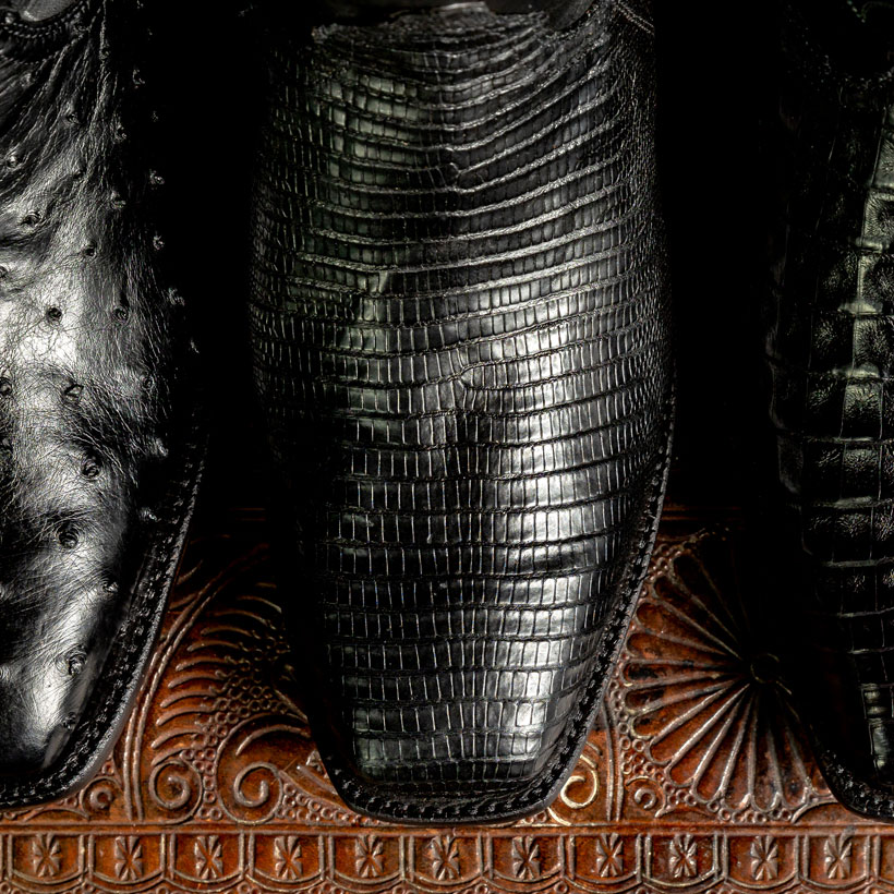 Three black boots with square toes posed on a brown leather piece.