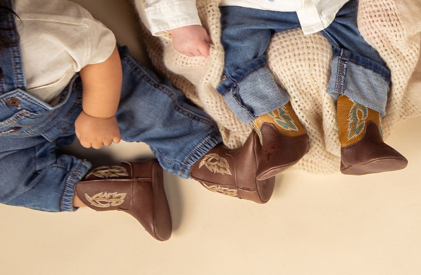 A group of infants wearing Justin Baby Canter in walnut (brown), Justin Baby Canter in pecan (tan), Justin Baby Canter in cognac (brown), Justin Bea in Arctic (white) an the Justin Baby Canter in cocoa (brown).