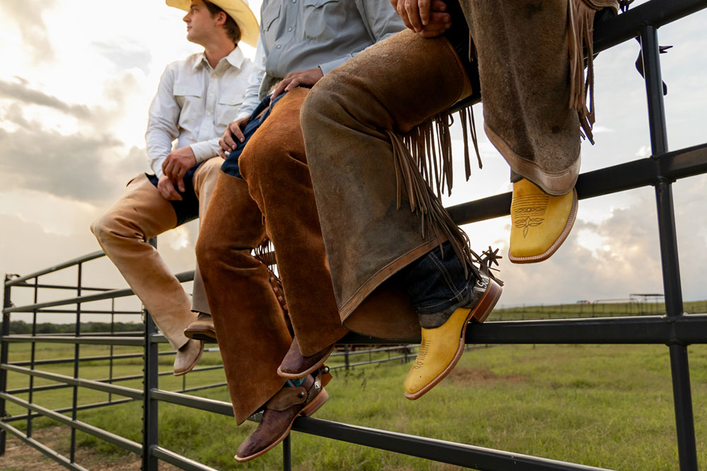 Three men sitting on a metal fence wearing Men’s CPX Western boots.