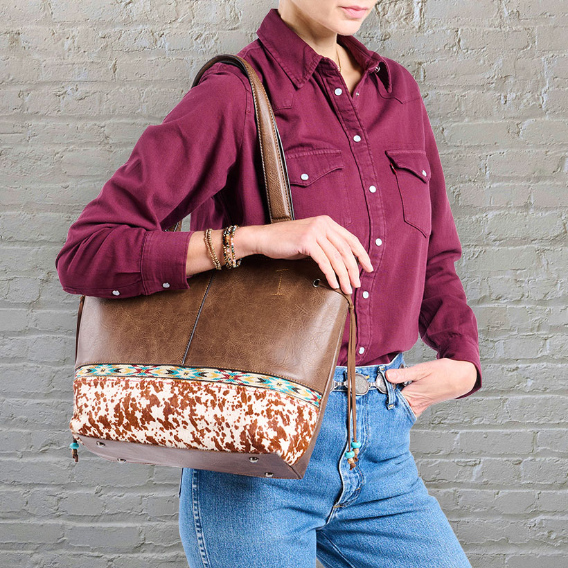 Women’s hair on tote bag being worn by a model wearing a red western pearl snap and jeans in front of a blank wall. 