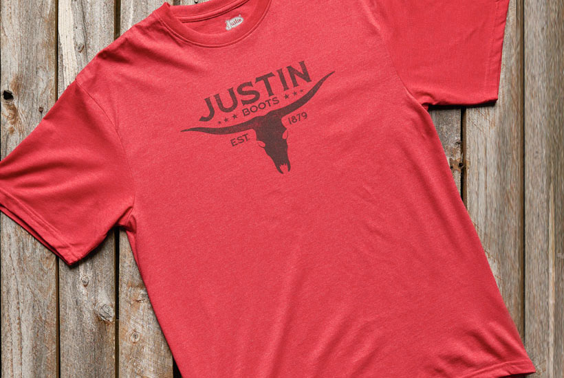 Justin men’s Bull Skull Tee in red laid on a wooden background.