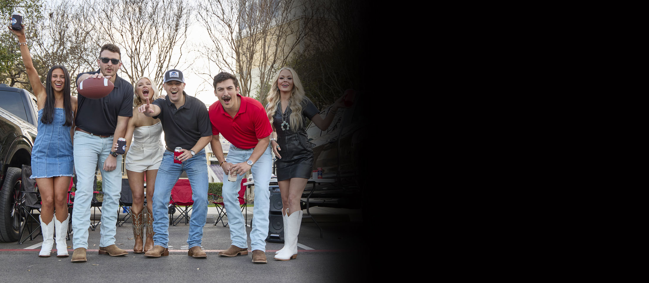 A group of young men and women tailgating between trucks, wearing Justin Boots.