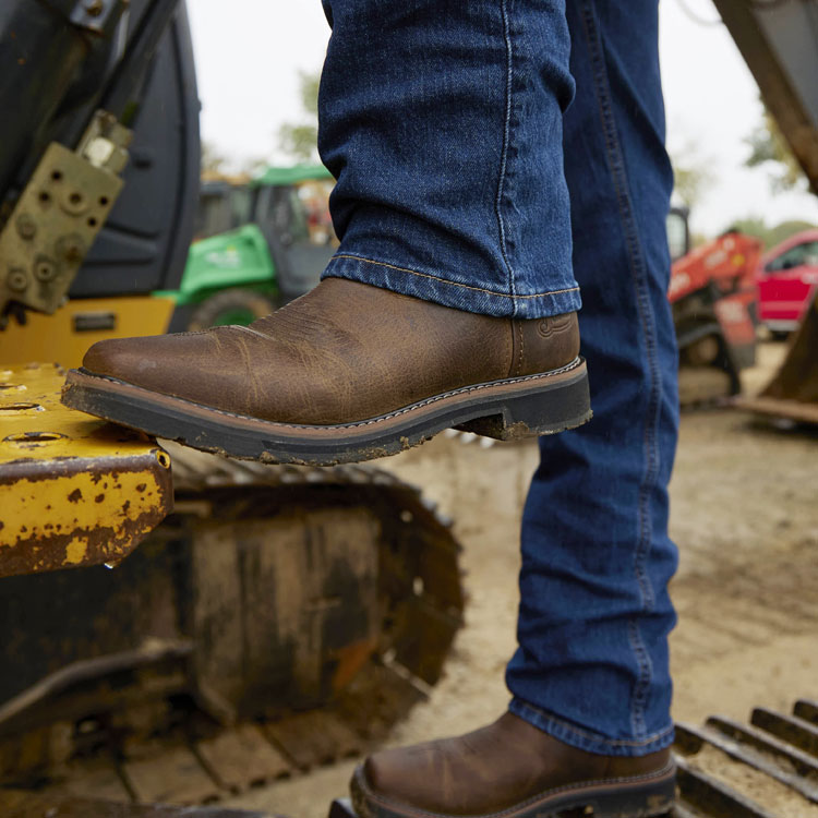 A man wearing the Driller 11” work boot in brown with his foot on a front end loader. 